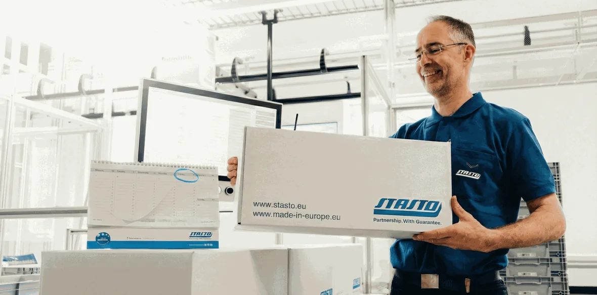 A STASTO employee with a package ready to ship, in front of the schedule